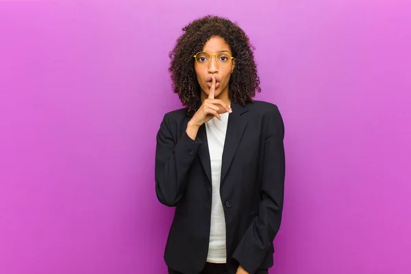 young black business woman asking for silence and quiet, gesturing with finger in front of mouth, saying shh or keeping a secret