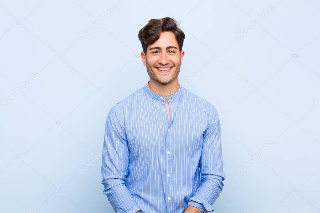 young handsome man with a big, friendly, carefree smile, looking positive, relaxed and happy, chilling against blue background