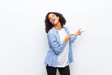 Genç, havalı, afro-amerikan kadın kendini neşeli ve şaşırmış hissediyor, şok olmuş bir ifadeyle gülümsüyor ve bir tarafı işaret ediyor.