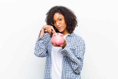 Beyaz duvarda kumbarası olan genç, güzel siyah bir kadın.