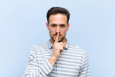 Genç ve yakışıklı adam ciddi görünüyor ve parmaklarını dudaklarına bastırıp sessizlik ya da sessizlik talep ediyor, sır saklıyor.