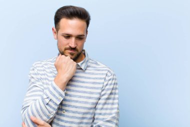 Genç yakışıklı adam ciddi, düşünceli ve endişeli, elleri çenesine bastırılmış, yan bakıyor.