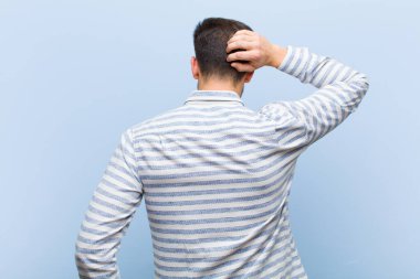 Genç yakışıklı adam düşünüyor ya da şüphe ediyor, kafasını kaşıyor, şaşkın ve kafası karışık hissediyor, arkaya ya da arkaya bakıyor.