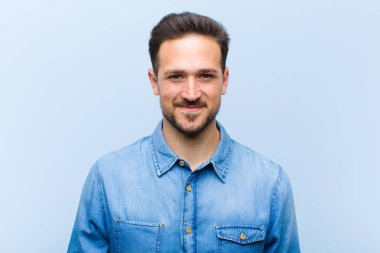 Genç yakışıklı adam pozitif ve kendinden emin gülümsüyor. Tatmin olmuş, arkadaş canlısı ve mutlu görünüyor.