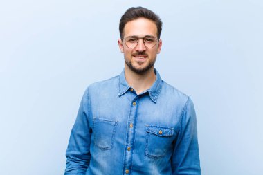 Genç ve yakışıklı bir adam neşeli, neşeli, mutlu, kendinden emin ve rahat bir ifadeyle gülümsüyor.