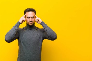 Genç yakışıklı adam, kafası karışık ya da şüpheci, bir fikre odaklanmış, çok düşünüyor, turuncu duvara karşı uzayı kopyalamak istiyor.