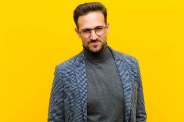 Genç yakışıklı adam gururlu, kendinden emin, havalı, küstah ve küstah görünüyor, gülümsüyor, turuncu duvara karşı başarılı hissediyor.