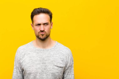 Kafası karışmış, kafası karışmış, bir sorunu çözmeye çalışan ya da turuncu duvara karşı düşünen genç yakışıklı bir adam.