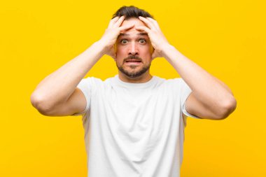 Dehşete kapılmış ve şok olmuş hisseden genç yakışıklı adam, turuncu duvara karşı ellerini kaldırıyor ve panikliyor.