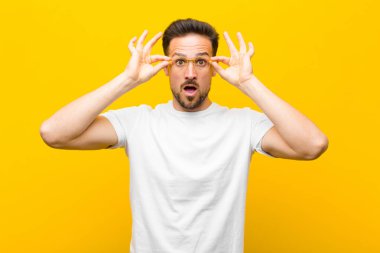 Genç yakışıklı adam şok olmuş, şaşırmış ve şaşırmış hissediyor. Elinde turuncu duvara bakan hayret verici, inanmayan bir bakış var.