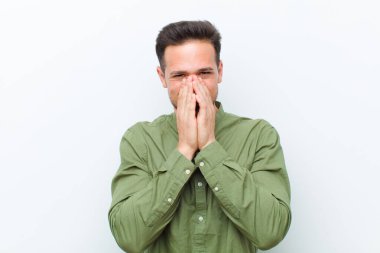 Genç yakışıklı adam mutlu, neşeli, şanslı ve şaşkın görünüyor. İki eliyle ağzını kapatıyor.