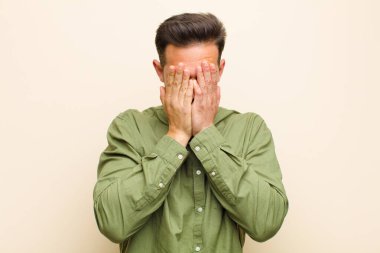 Genç yakışıklı adam üzgün, hayal kırıklığına uğramış, gergin ve depresif, iki eliyle yüzünü kaplayan, ağlayan