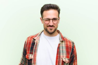 Genç yakışıklı adam mutlu ve arkadaş canlısı görünüyor, gülümsüyor ve sana olumlu bir tavırla göz kırpıyor.