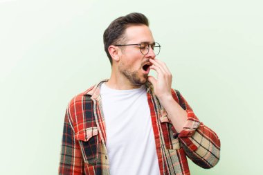 Genç yakışıklı adam tembelce esniyor, uykulu, yorgun ve sıkkın görünüyor.