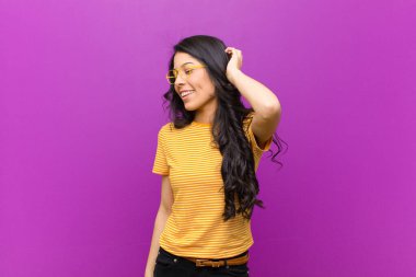 Genç, güzel, Latin bir kadın neşe içinde gülümsüyor. Morarmış duvara karşı olumlu, mutlu ve kendinden emin bir bakışla yumruk yumruğa bakıyor.