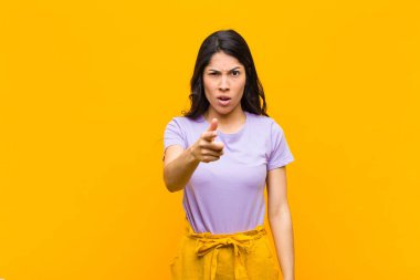 Kızgın agresif bir ifadeyle kameraya bakan genç, güzel Latin bir kadın turuncu duvara karşı öfkeli, çılgın bir patron gibi görünüyor.