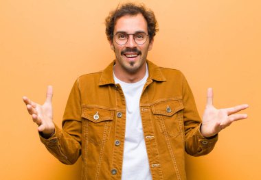 Genç yakışıklı adam kendini mutlu, şaşkın, şanslı ve şaşırmış hissediyor. Turuncu duvara karşı inanılmaz.