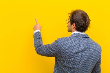 Genç yakışıklı adam dikiliyor ve fotokopi alanındaki objeyi işaret ediyor, turuncu duvara karşı dikiz manzaralı.