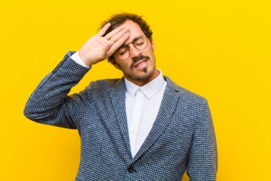 Genç yakışıklı adam stresli, yorgun ve hayal kırıklığına uğramış görünüyor. Alnından ter akıyor. Turuncu duvara karşı umutsuz ve bitkin hissediyor.