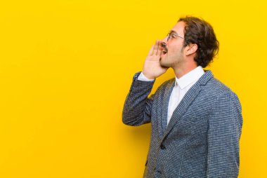 Genç yakışıklı profil görüntüsü, mutlu ve heyecanlı görünüyor, bağırıyor ve turuncu duvara karşı alanı kopyalamak için çağırıyor.