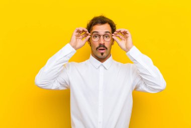 Genç yakışıklı adam şok olmuş, şaşırmış ve şaşırmış hissediyor. Elinde turuncu duvara bakan hayret verici, inanmayan bir bakış var.