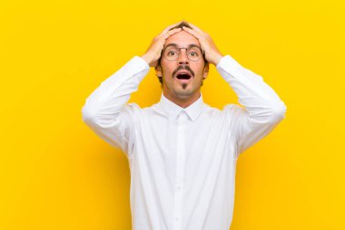 Dehşete kapılmış ve şok olmuş hisseden genç yakışıklı adam, turuncu duvara karşı ellerini kaldırıyor ve panikliyor.