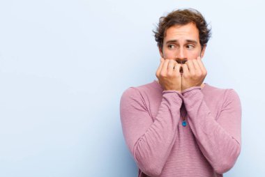 Genç yakışıklı adam endişeli, gergin, stresli ve korkmuş görünüyor, tırnaklarını yiyor ve düz duvara izole edilmiş yanal fotokopi odasına bakıyor.