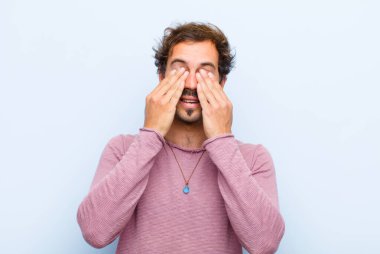 Genç yakışıklı adam gülümsüyor ve mutlu hissediyor, iki eliyle gözlerini kapatıyor ve duvara yaslanmış inanılmaz bir sürprizi bekliyor.