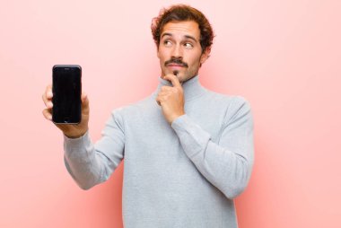 Pembe düz duvara karşı akıllı telefonu olan genç ve yakışıklı bir adam.