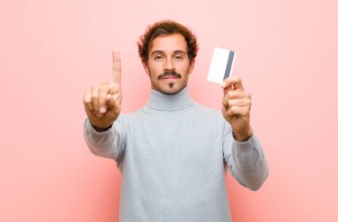 Pembe düz duvara karşı kredi kartı olan genç ve yakışıklı bir adam.