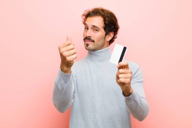 Pembe düz duvara karşı kredi kartı olan genç ve yakışıklı bir adam.