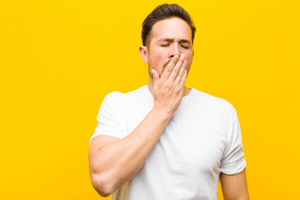 young handsome man yawning lazily early in the morning, waking and looking sleepy, tired and bored against orange wall