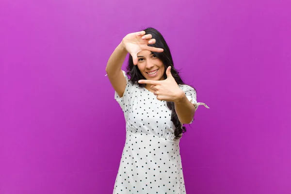 若いラテン系の女性は幸せを感じます フレンドリーで肯定的です 笑顔と紫色の壁に手で肖像画や写真フレームを作ります — ストック写真
