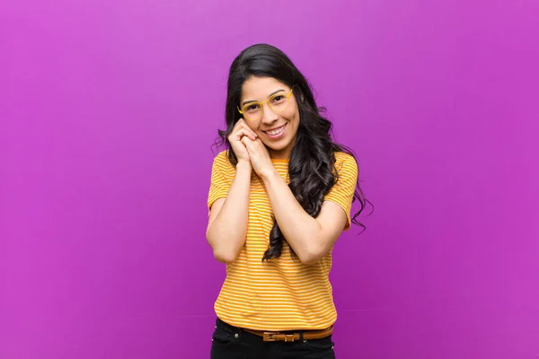 可愛いラテン系の若い女性が愛を感じ 可愛くて可愛くて幸せそうな顔をして 紫色の壁に向かい合って手でロマンチックな笑顔をして — ストック写真