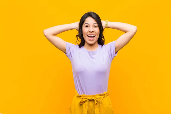 young pretty latin woman looking happy, carefree, friendly and relaxed enjoying life and success, with a positive attitude against orange wall