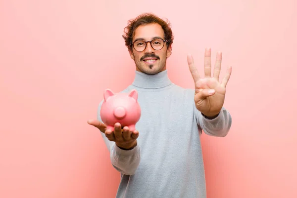 Joven Hombre Guapo Con Una Alcancía Contra Pared Plana Rosa — Foto de Stock