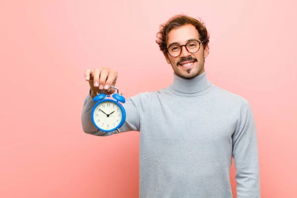 young handsome man with an alarm clock against pink flat wall