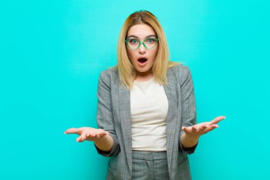 Genç ve güzel sarışın kadın ağzı açık ve şaşırmış, şaşırmış ve şaşırmış bir şekilde düz duvara karşı inanılmaz bir sürprizle