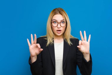 Genç, güzel, sarışın kadın şok olmuş, şaşırmış ve şaşırmış hissediyor. Onaylıyor. İki elini de duvara yaslayarak işaret veriyor.