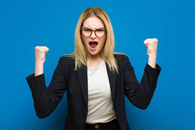 Genç ve güzel sarışın bir kadın sinirli bir ifadeyle ya da yumruklarıyla düz duvara karşı başarıyı kutlarken agresif bir şekilde bağırıyor.