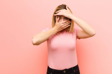 Genç ve güzel sarışın kadın kameraya hayır diyen iki eliyle yüzünü kapatıyor! Resimleri reddetmek veya pembe düz duvara yaslanan fotoğrafları yasaklamak