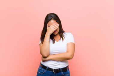 Genç, güzel, İspanyol bir kadın stresli, utanmış ya da üzgün görünüyor. Başı ağrıyor, yüzü pembe duvara değiyor.