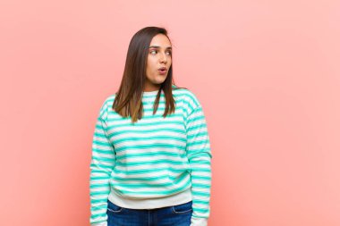 Genç, güzel İspanyol kadın şok olmuş, mutlu, şaşkın ve şaşırmış hissediyor. Ağzı açık pembe duvara bakıyor.