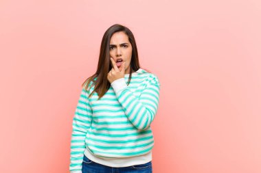 Ağzı ve gözleri sonuna kadar açık, elleri çenesinde, hoş olmayan bir şekilde şokta olan, pembe duvara karşı ne ya da vay canına diyen genç, İspanyol bir kadın.