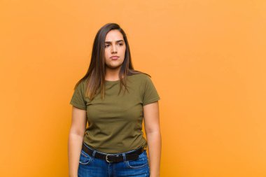 Genç, güzel bir kadın üzgün, üzgün ya da kızgın ve olumsuz bir tavır takınıyor. Turuncu duvara karşı anlaşmazlık içinde somurtuyor.