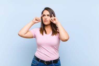 Genç, güzel bir kadın, kafası karışmış ya da şüpheye düşmüş, bir fikre odaklanmış, çok düşünüyor, mavi arkaplana karşı uzayı kopyalamak istiyor.