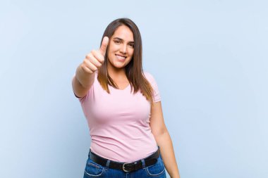 Genç, güzel bir kadın gururlu, tasasız, kendinden emin ve mutlu, mavi arka planda olumlu gülümsüyor.