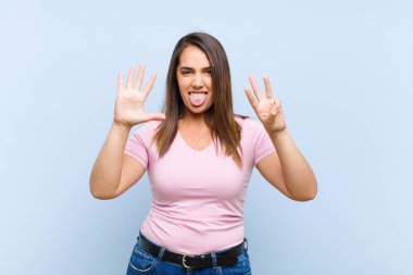 Genç ve güzel bir bayan gülümsüyor ve arkadaş canlısı görünüyor, 8 ya da 8 numarayı gösteriyor, mavi arka planda geriye doğru sayıyor.