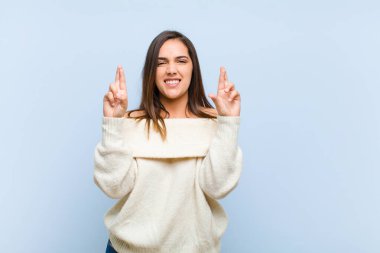 Genç ve güzel bir kadın gergin ve umutlu, dua ediyor ve mavi arka planda iyi şanslar diliyor.