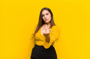 Genç, güzel bir kadın kızgın, sinirli, isyankar ve agresif orta parmağını sallayarak turuncu duvara karşı mücadele ediyor.